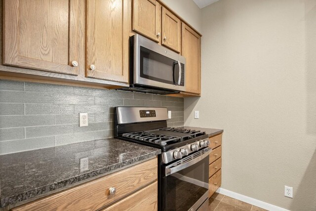 kitchen featuring appliances with stainless steel finishes, dark stone countertops, backsplash, and light tile patterned floors