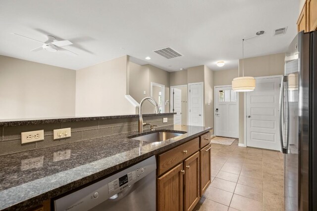 kitchen with hanging light fixtures, stainless steel appliances, dark stone countertops, ceiling fan, and sink