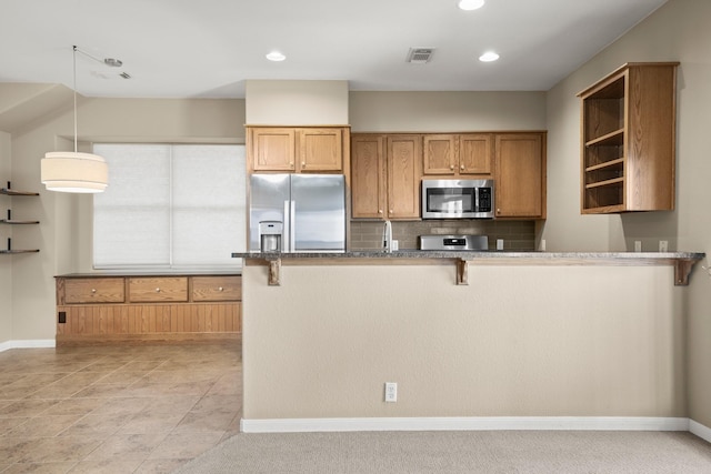 kitchen featuring a kitchen bar, dark stone countertops, kitchen peninsula, hanging light fixtures, and appliances with stainless steel finishes