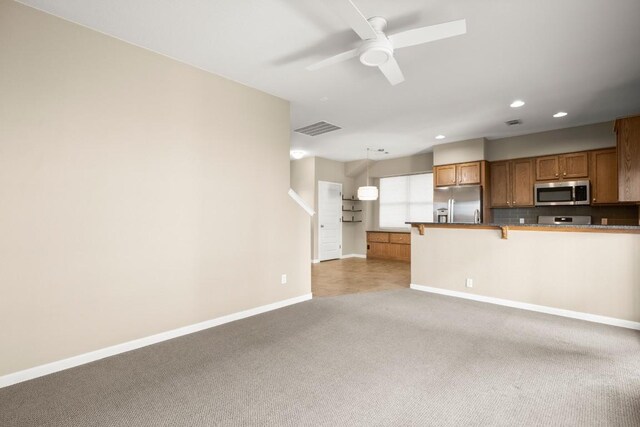 kitchen featuring appliances with stainless steel finishes, light carpet, hanging light fixtures, and a kitchen bar