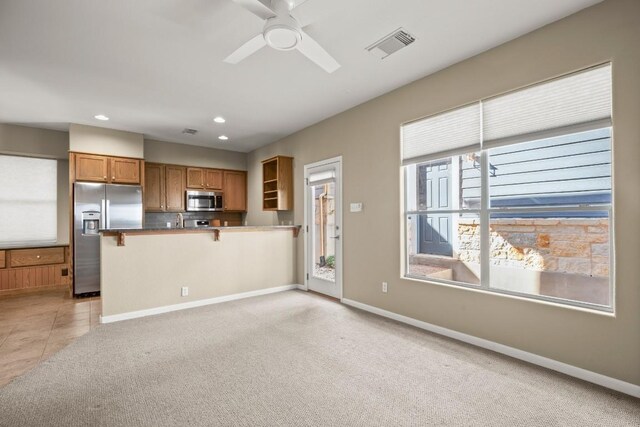 kitchen with kitchen peninsula, a kitchen bar, light colored carpet, appliances with stainless steel finishes, and ceiling fan