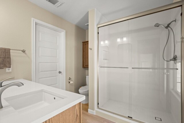 bathroom with toilet, hardwood / wood-style flooring, a shower with shower door, and vanity