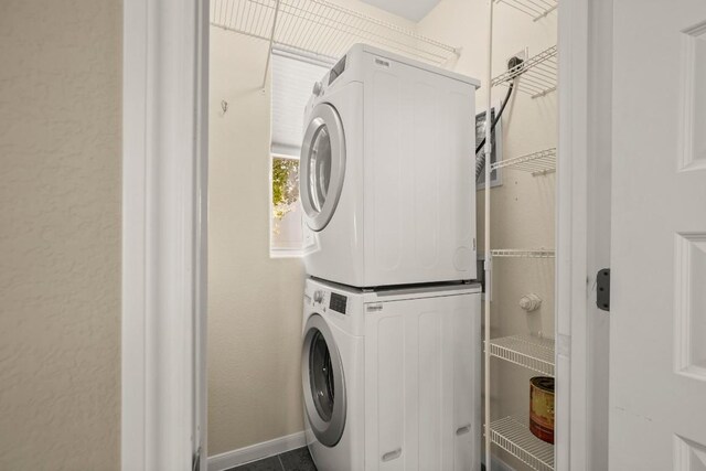 laundry area featuring stacked washer / dryer and dark tile patterned flooring