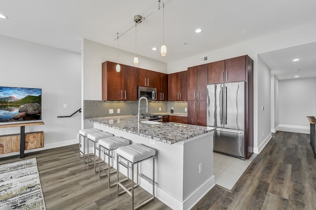 kitchen featuring stainless steel appliances, backsplash, hanging light fixtures, kitchen peninsula, and light stone counters