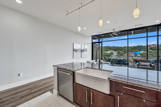 kitchen with pendant lighting, stainless steel dishwasher, sink, a wall of windows, and light stone counters