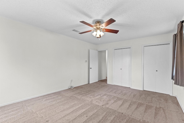 unfurnished bedroom with a textured ceiling, ceiling fan, light colored carpet, and multiple closets