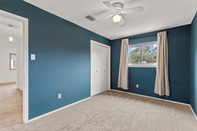 unfurnished bedroom with ceiling fan, light colored carpet, a textured ceiling, and a closet