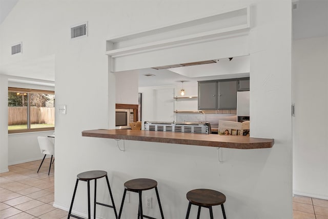 kitchen featuring light tile patterned floors, a kitchen bar, backsplash, and gray cabinets