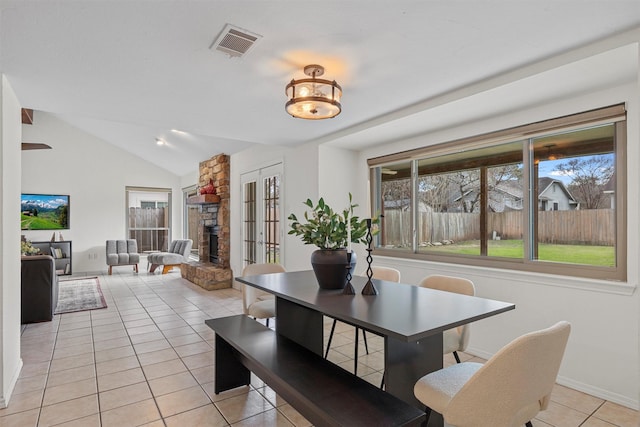 tiled dining room featuring lofted ceiling and a stone fireplace