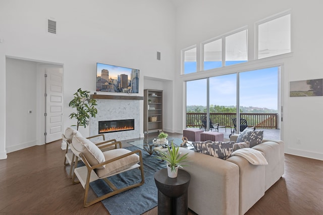 living room with a towering ceiling, dark hardwood / wood-style flooring, a large fireplace, and built in shelves