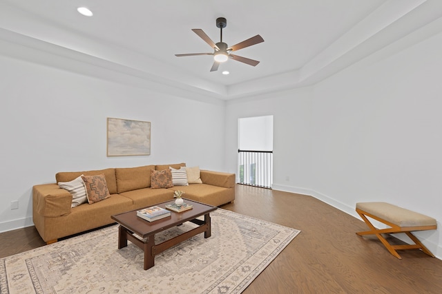 living room with hardwood / wood-style floors, a raised ceiling, and ceiling fan