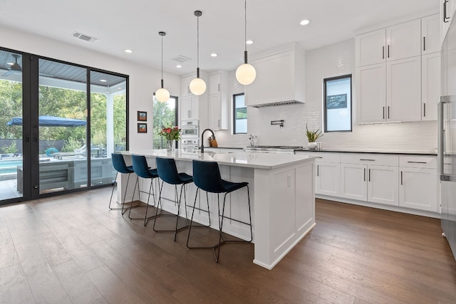 kitchen featuring visible vents, white cabinets, decorative backsplash, an island with sink, and dark wood-style flooring