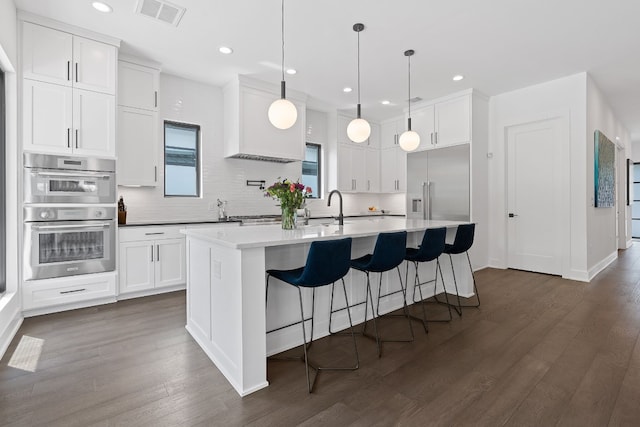 kitchen with stainless steel appliances, visible vents, decorative backsplash, white cabinetry, and an island with sink