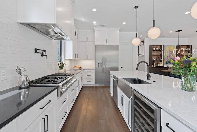 kitchen with beverage cooler, stainless steel appliances, premium range hood, light stone countertops, and dark wood finished floors