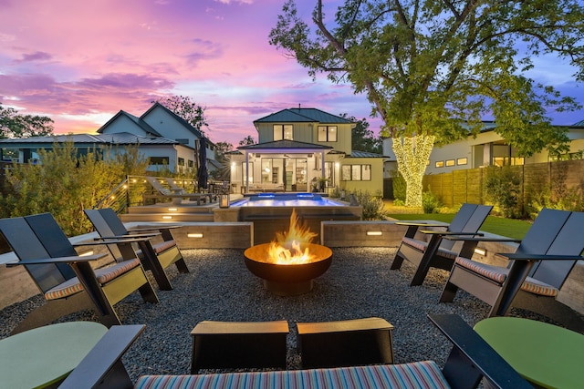 patio terrace at dusk with fence, a fire pit, and an outdoor pool