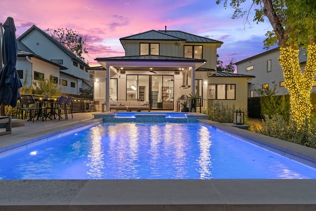 back of property at dusk featuring metal roof, a standing seam roof, fence, a patio area, and a pool with connected hot tub