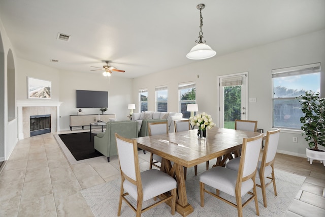 tiled dining space featuring a fireplace, ceiling fan, and plenty of natural light