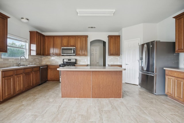 kitchen with appliances with stainless steel finishes, tasteful backsplash, a center island, and sink