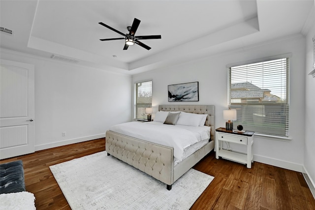 bedroom featuring dark wood-type flooring, a raised ceiling, ceiling fan, and crown molding