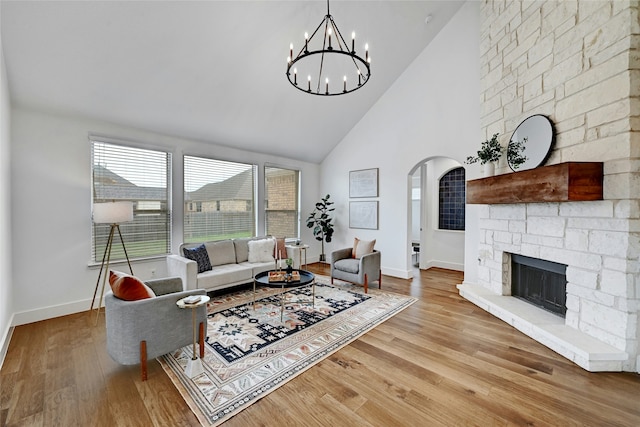 living room featuring high vaulted ceiling, an inviting chandelier, light hardwood / wood-style floors, and a stone fireplace