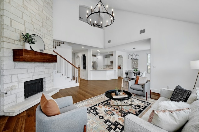 living room featuring hardwood / wood-style floors, a stone fireplace, a towering ceiling, and a chandelier