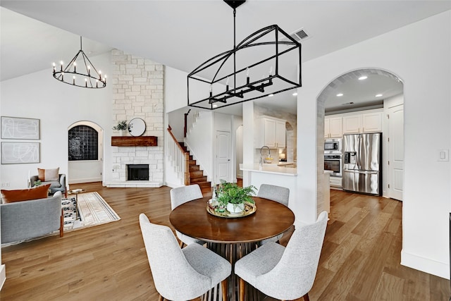 dining space with sink, light wood-type flooring, vaulted ceiling, and a fireplace