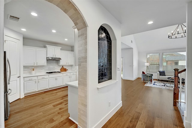 kitchen featuring gas cooktop, light hardwood / wood-style floors, decorative backsplash, white cabinetry, and stainless steel refrigerator