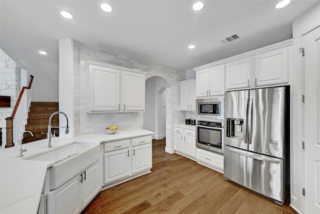 kitchen with stainless steel appliances, sink, white cabinets, light hardwood / wood-style flooring, and backsplash