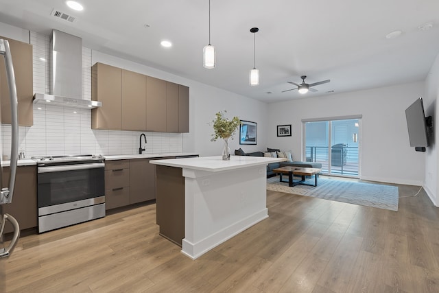 kitchen featuring decorative light fixtures, wall chimney range hood, a kitchen island, ceiling fan, and stainless steel range with electric stovetop