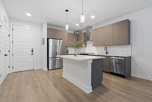 kitchen featuring stainless steel appliances, decorative light fixtures, wall chimney exhaust hood, tasteful backsplash, and an island with sink