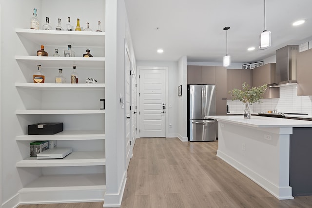 kitchen with a kitchen breakfast bar, light hardwood / wood-style floors, stainless steel refrigerator, wall chimney range hood, and pendant lighting