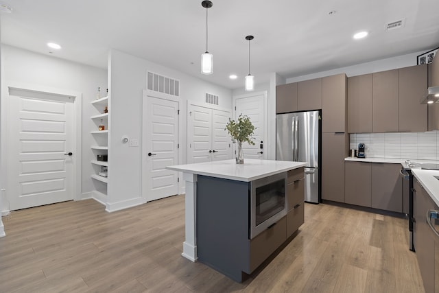 kitchen featuring a center island, stainless steel refrigerator, hanging light fixtures, gray cabinets, and built in microwave