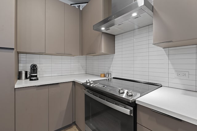 kitchen featuring electric stove, gray cabinets, wall chimney range hood, and tasteful backsplash