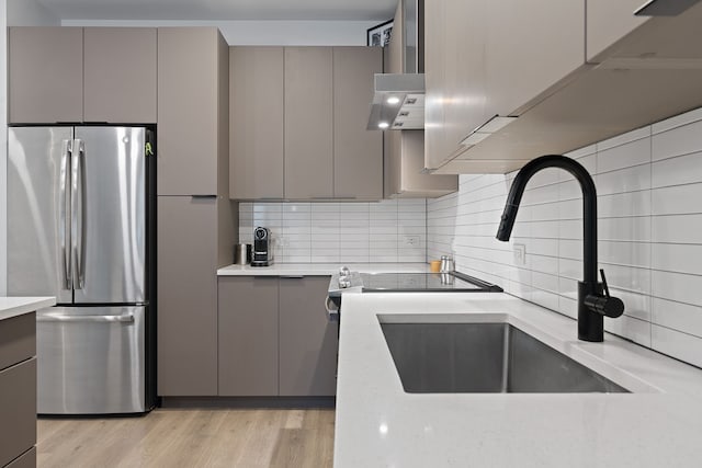 kitchen with stainless steel fridge, light hardwood / wood-style floors, gray cabinets, backsplash, and sink