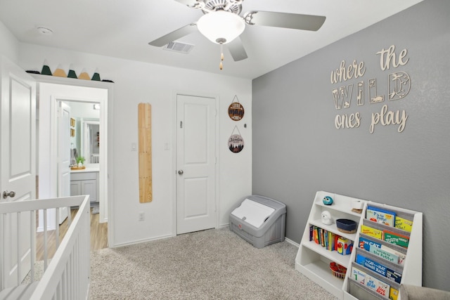 carpeted bedroom with ceiling fan and a crib