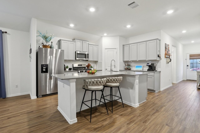 kitchen featuring stainless steel appliances, a center island with sink, dark hardwood / wood-style flooring, a kitchen breakfast bar, and sink