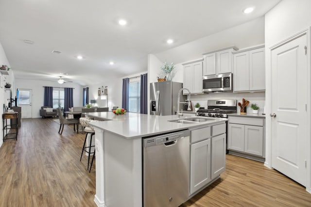 kitchen featuring stainless steel appliances, an island with sink, a kitchen bar, light wood-type flooring, and ceiling fan