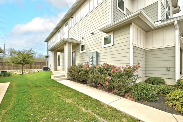 view of side of property with board and batten siding, a yard, central AC, and fence