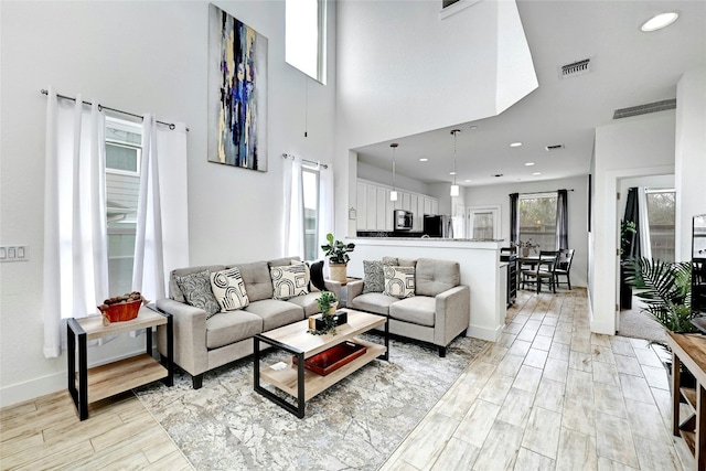 living area featuring light wood finished floors, recessed lighting, visible vents, a high ceiling, and baseboards