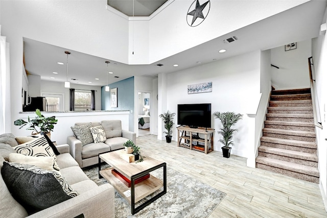 living area with visible vents, a towering ceiling, light wood-style flooring, stairway, and recessed lighting