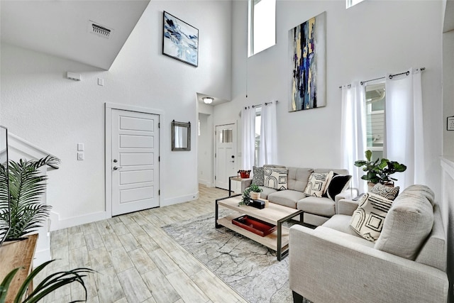 living room featuring light wood-style floors, a high ceiling, visible vents, and baseboards