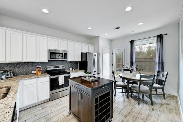 kitchen with tasteful backsplash, visible vents, light stone counters, stainless steel appliances, and white cabinetry