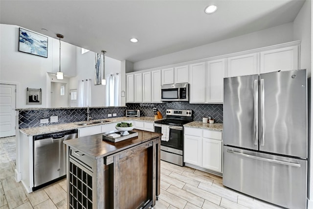 kitchen with appliances with stainless steel finishes, a sink, decorative light fixtures, and white cabinetry