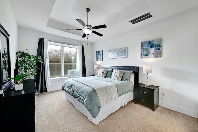 bedroom with light carpet, baseboards, visible vents, ceiling fan, and a tray ceiling