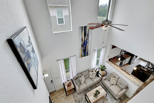 living room with light wood-type flooring, ceiling fan, a high ceiling, and a wealth of natural light