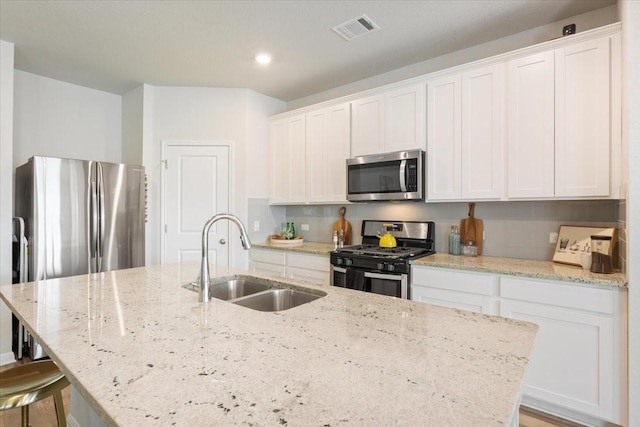 kitchen with white cabinets, appliances with stainless steel finishes, an island with sink, and sink