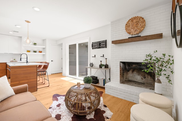 living room with a fireplace, light wood-type flooring, and sink