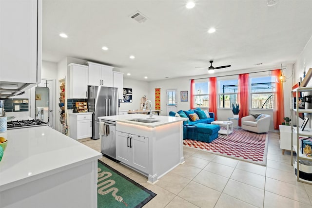 kitchen with stainless steel appliances, a kitchen island with sink, white cabinets, light tile patterned flooring, and sink