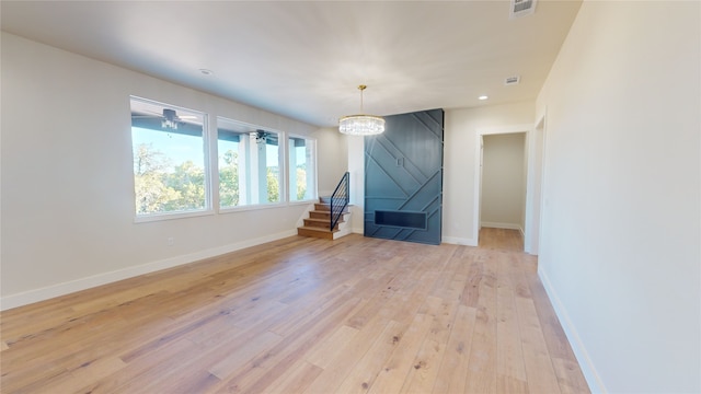 unfurnished living room featuring baseboards, visible vents, stairs, light wood-type flooring, and a chandelier