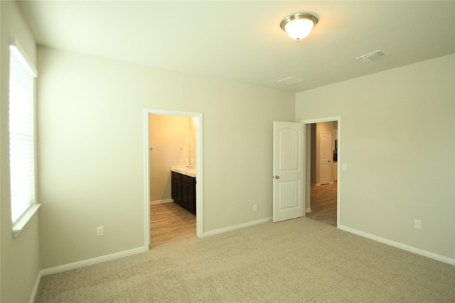 unfurnished bedroom with ensuite bathroom and light carpet